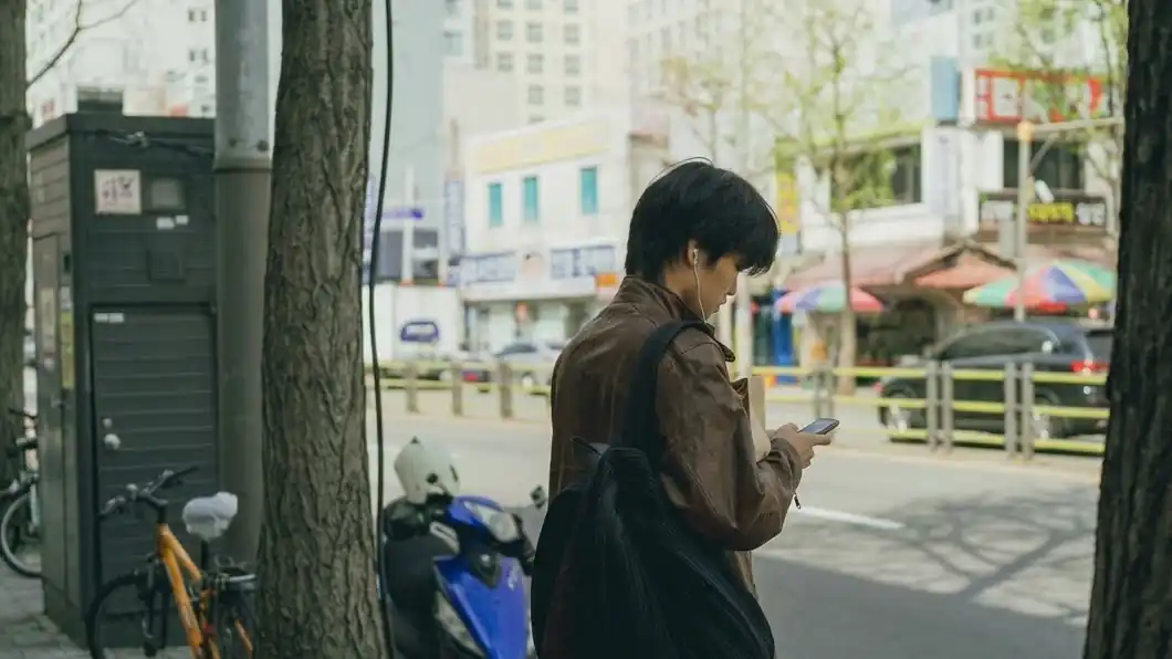 A traveler checking his phone on a tree-lined street in Seoul