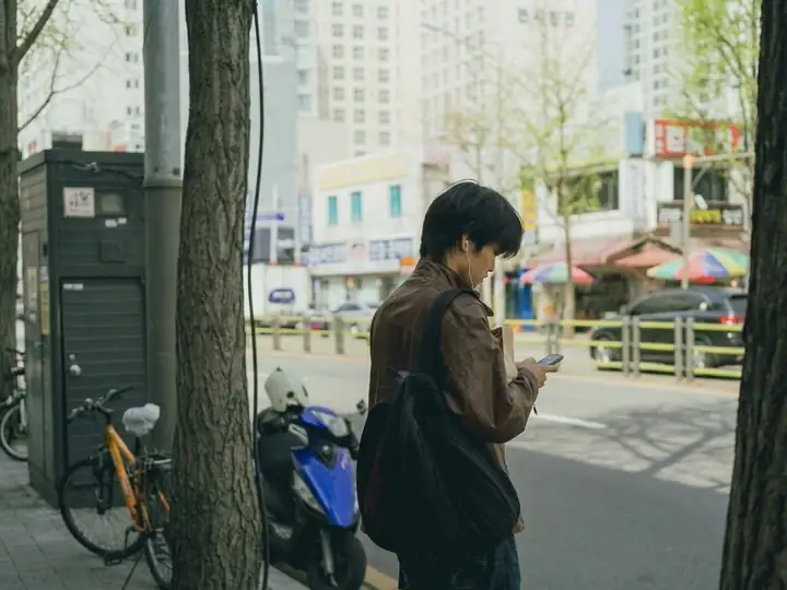 A traveler checking his phone on a tree-lined street in Seoul